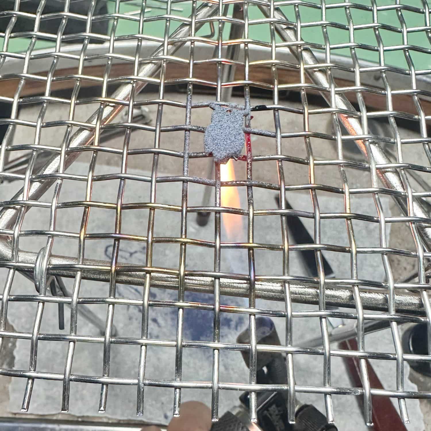 Gas torch firing enamel onto a brass charm on a steel mesh during TG Jewellery enamelling workshop
