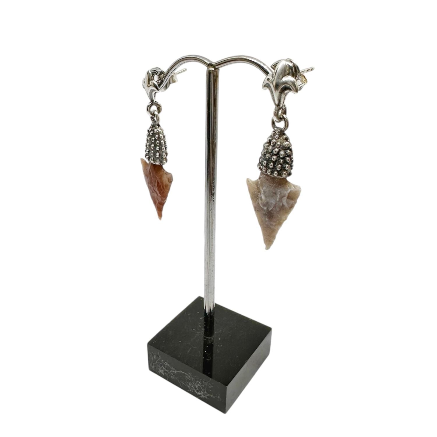 Pair of arrowhead-shaped earrings on a stand with a white background