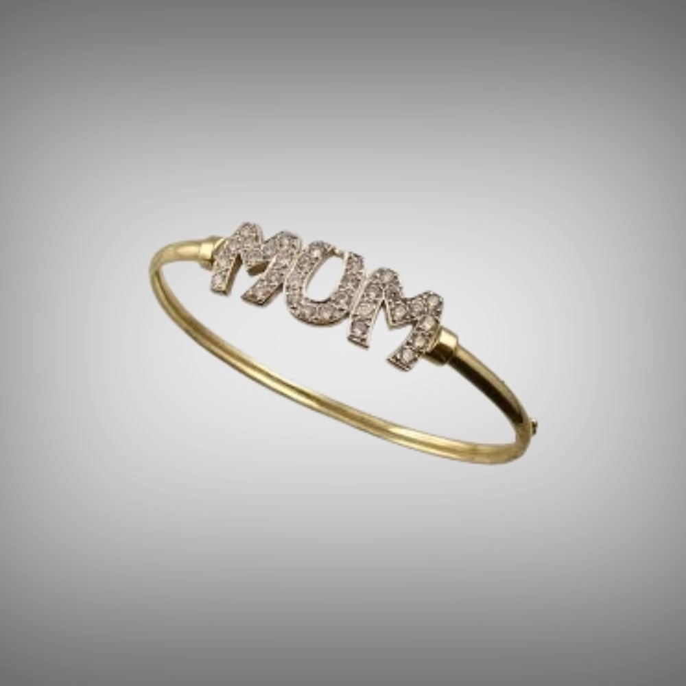A gold bangle bracelet featuring the word 'MUM' in raised letters paved with small diamonds, hand carved from Tg-Jewellery by Tamara Gervasio