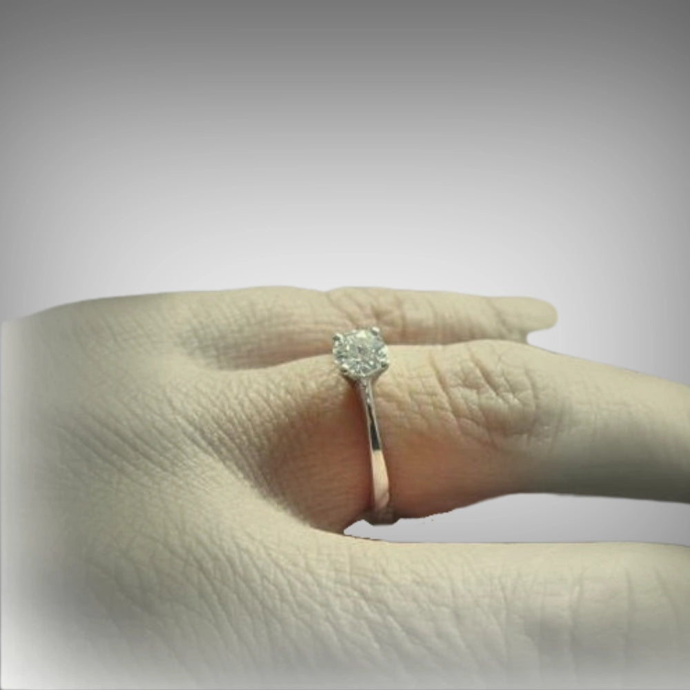 A classic solitaire engagement ring with a round brilliant-cut diamond on a slim 18ct white gold band, shown worn on a hand by Tg-Jewellery