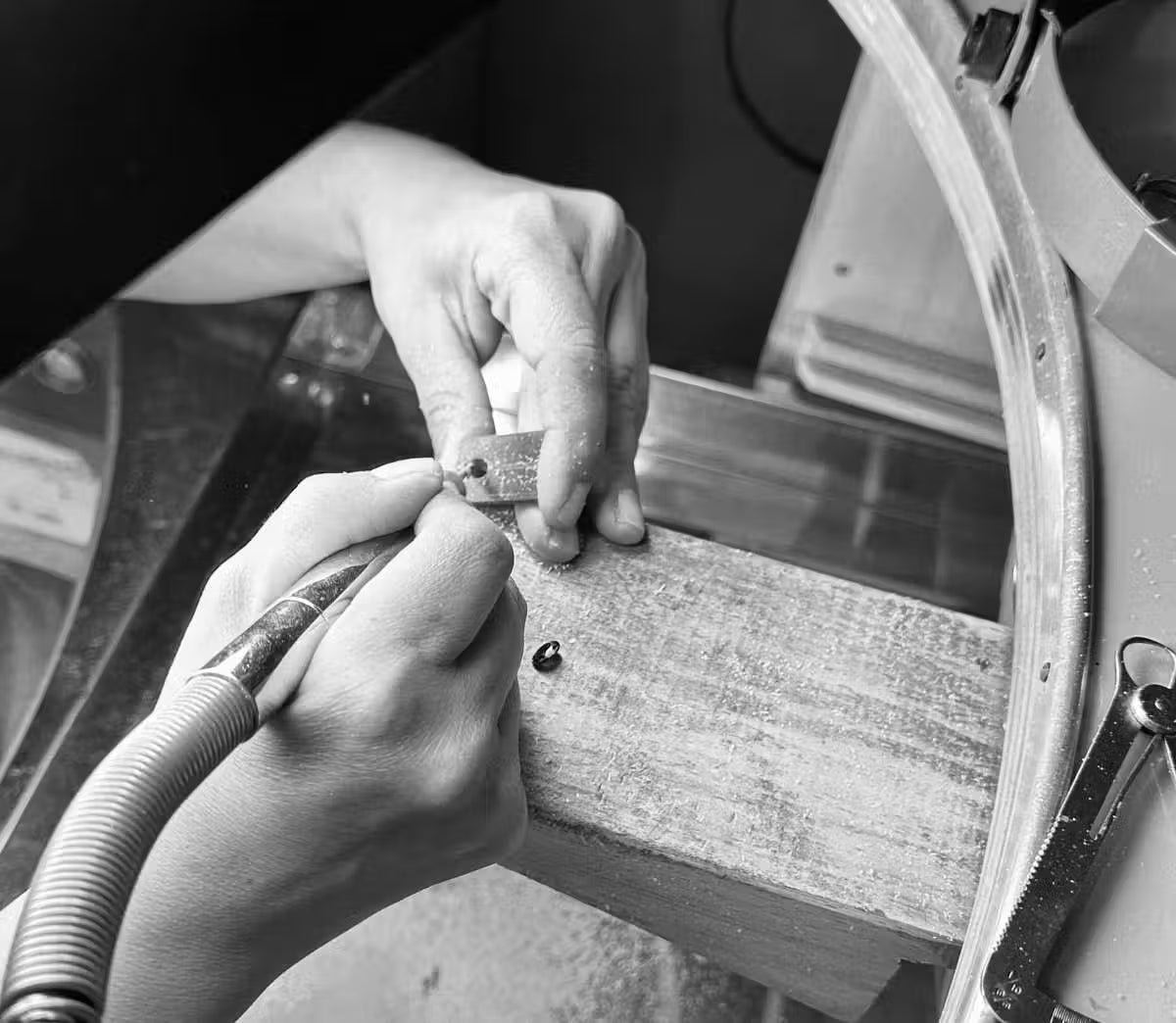 A close-up black and white photo of Tamara Gervasio hands using a handheld rotary tool to carve a  setting for a lost wax carving ring on a workbench.