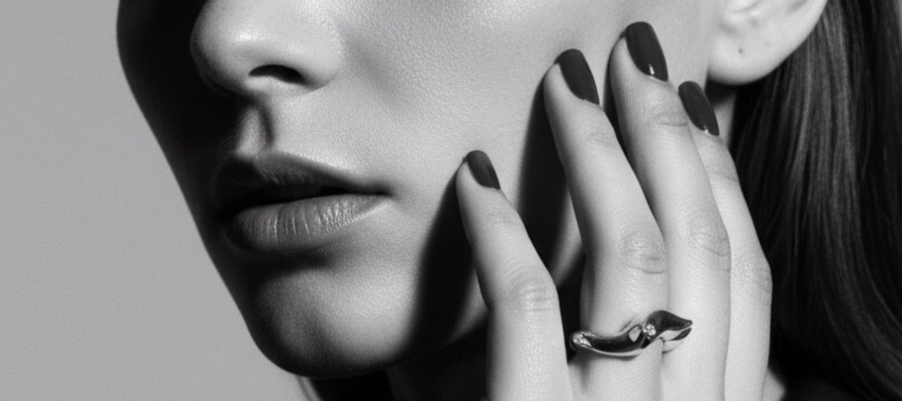 Close-up of a woman's face with a hand touching her cheek, wearing a ring.